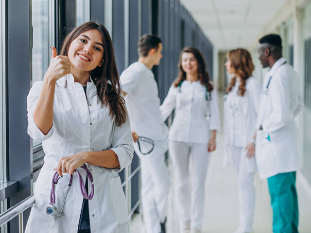young-female-doctor-with-thumbs-up-gesture-standing-corridor-hospital