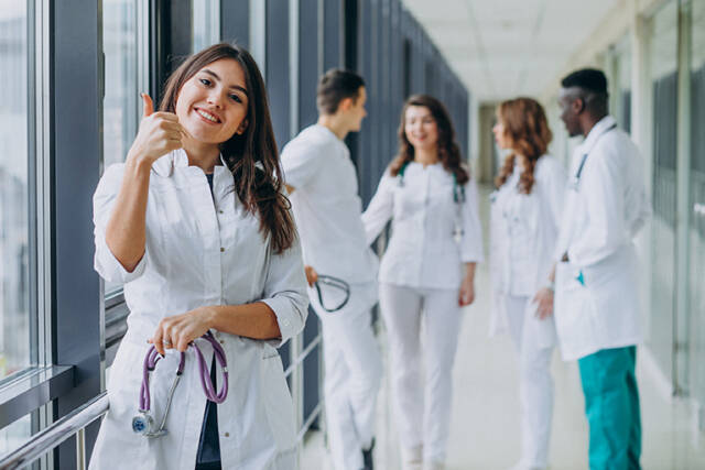 young-female-doctor-with-thumbs-up-gesture-standing-corridor-hospital